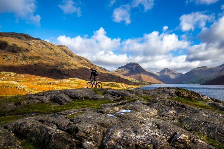 Ein Mountainbiker fährt während Yoga Retreat in den Bergen vor einer Bergkulisse an einem Bergsee vorbei